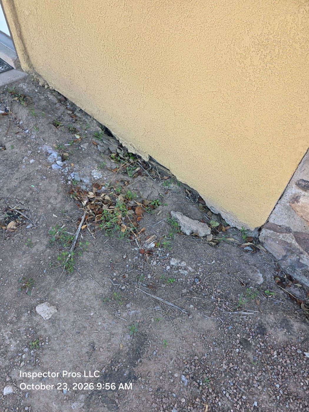 Soil eroded away from the base of a stucco wall exposing the slab edge
