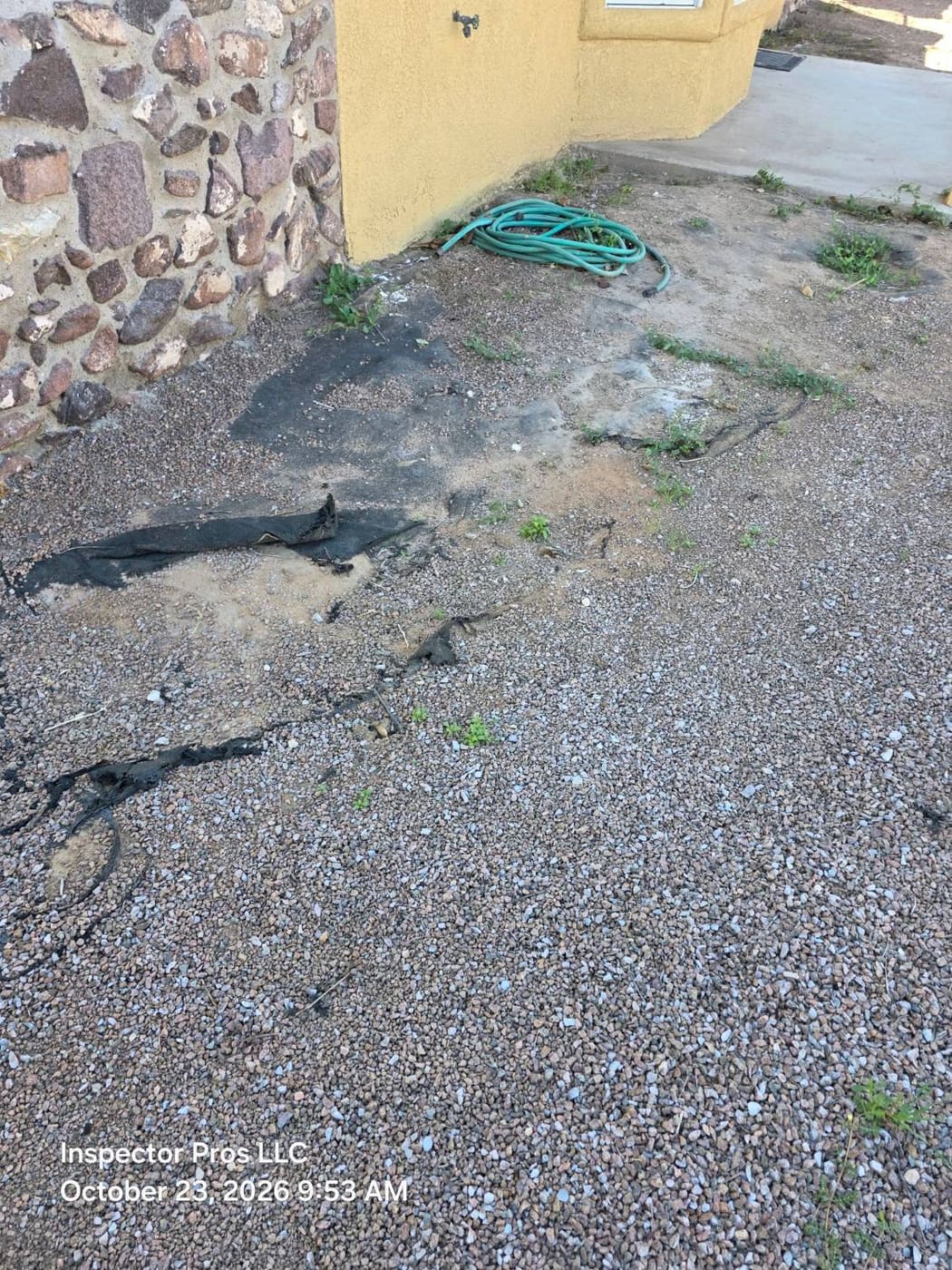 Erosion channels cut through gravel and landscape fabric beside a home