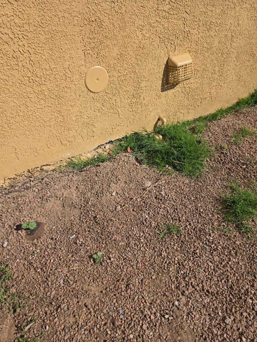 Ground sloping toward a stucco wall near a dryer vent and cleanout
