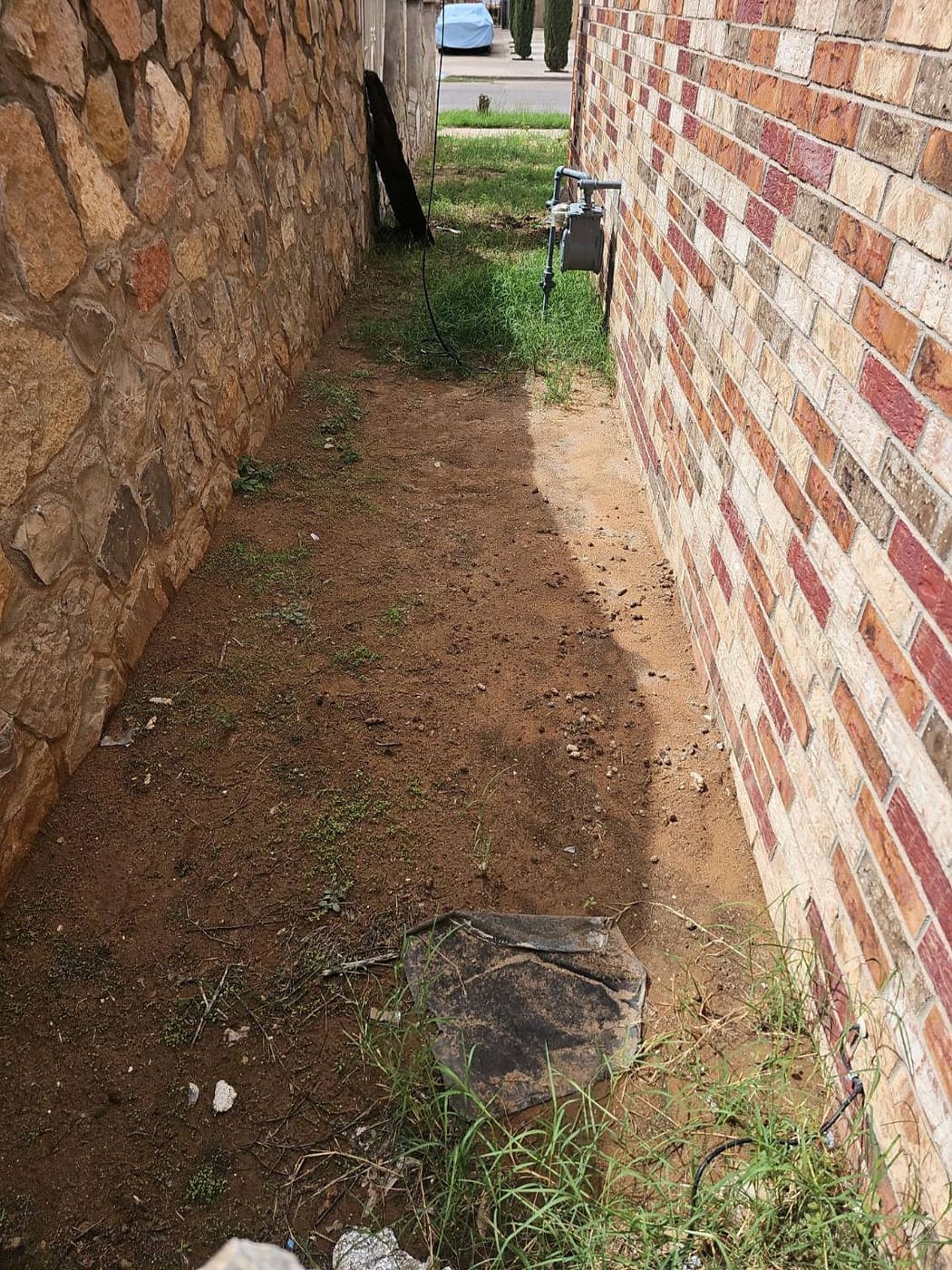 Narrow side yard between a brick home and a stone boundary wall in El Paso