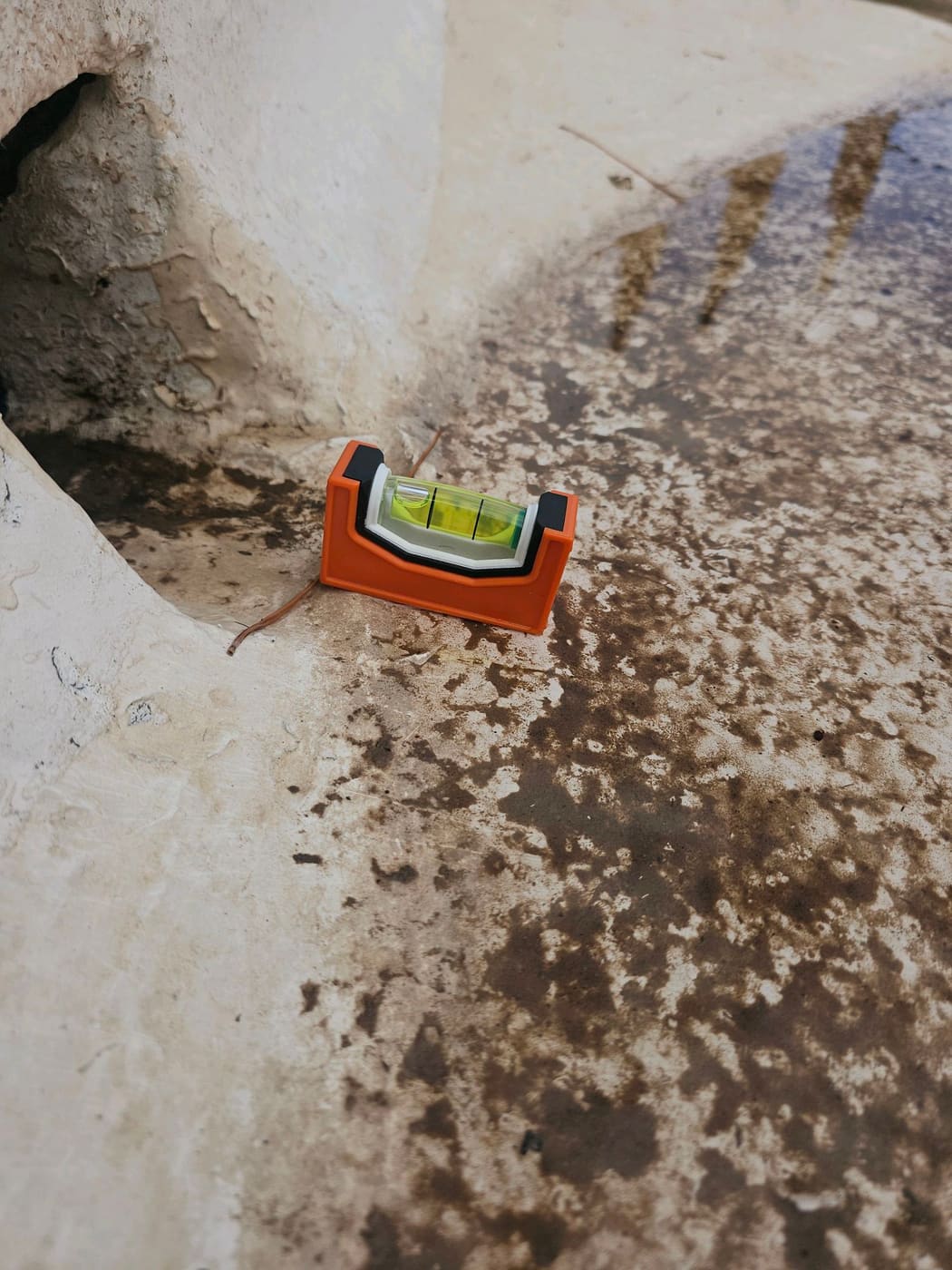 Level placed at a new construction scupper showing water pooled below the opening