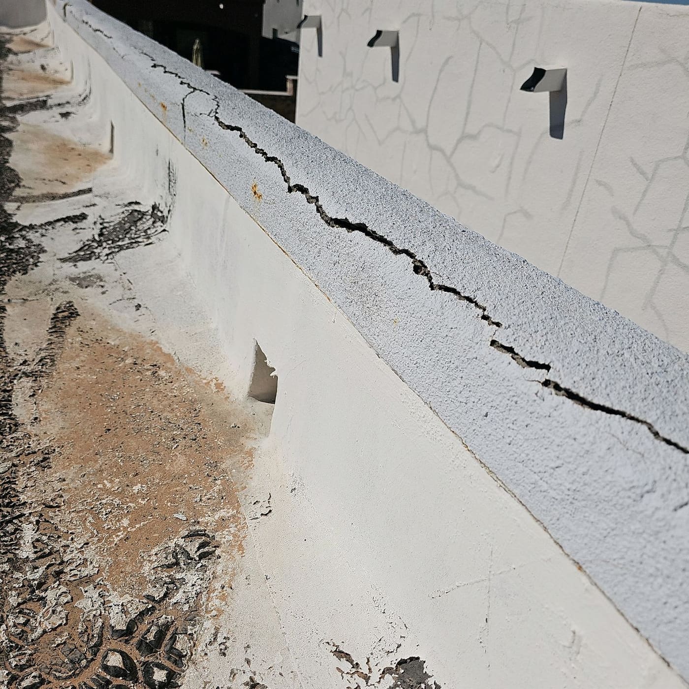 Long crack along a parapet cap with scupper openings at the roof line