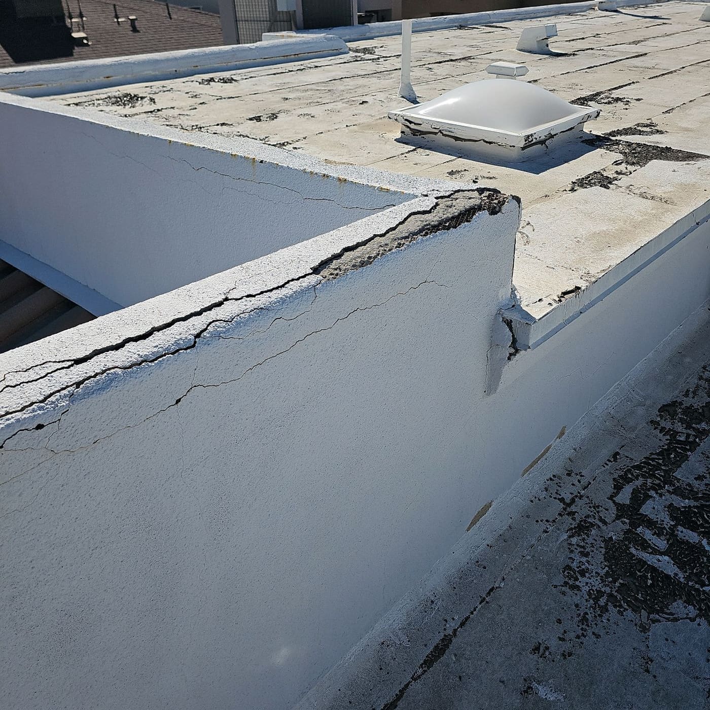 Cracked parapet corner and failing skylight seal on a flat roof