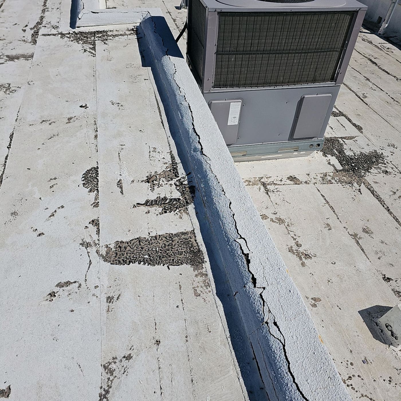 Cracked low parapet wall next to a rooftop air conditioning unit