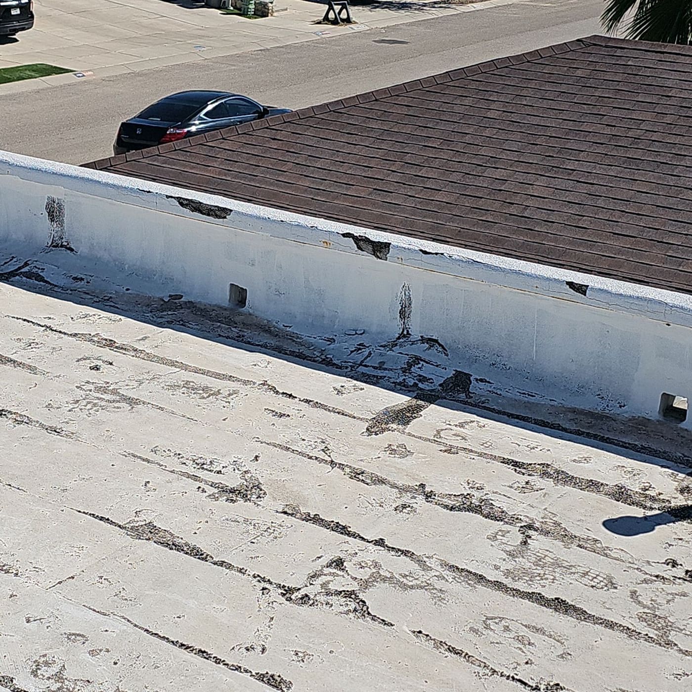 Inside face of a parapet wall with patched cracks and worn roofing at the base